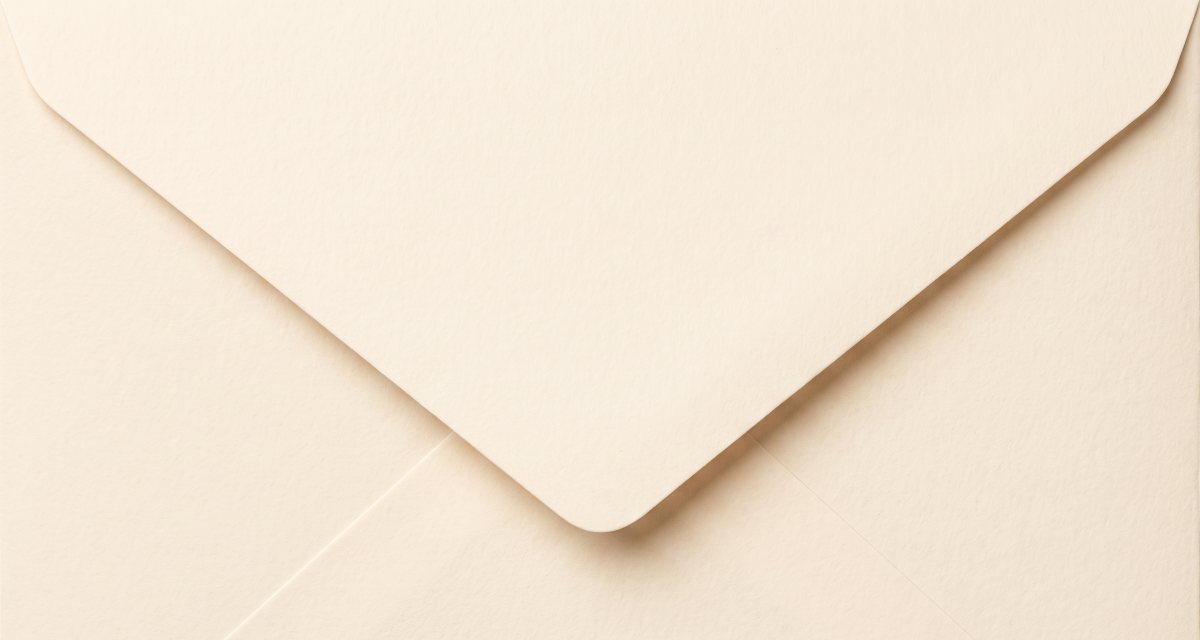 A blank cream envelope lying on a cream desk, flap closed, nothing written on it.